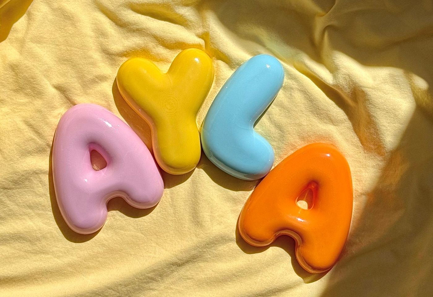 Glossy letters spelling AYLA in pink, yellow, blue and orange